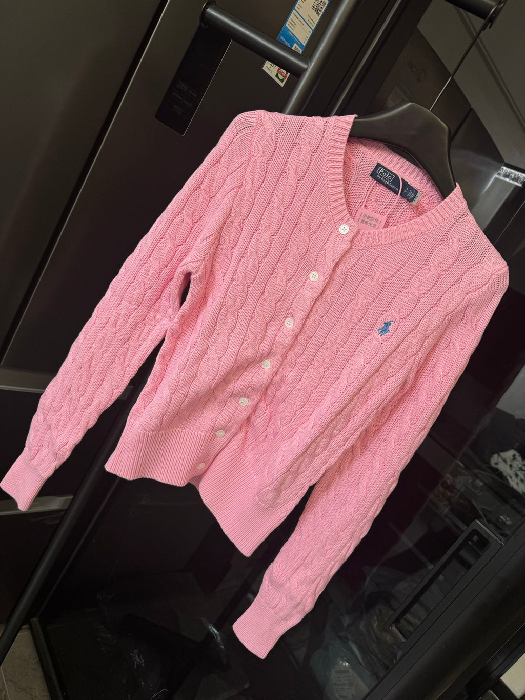 Pink cable-knit cardigan sweater with Polo logo and button placket, angled view.