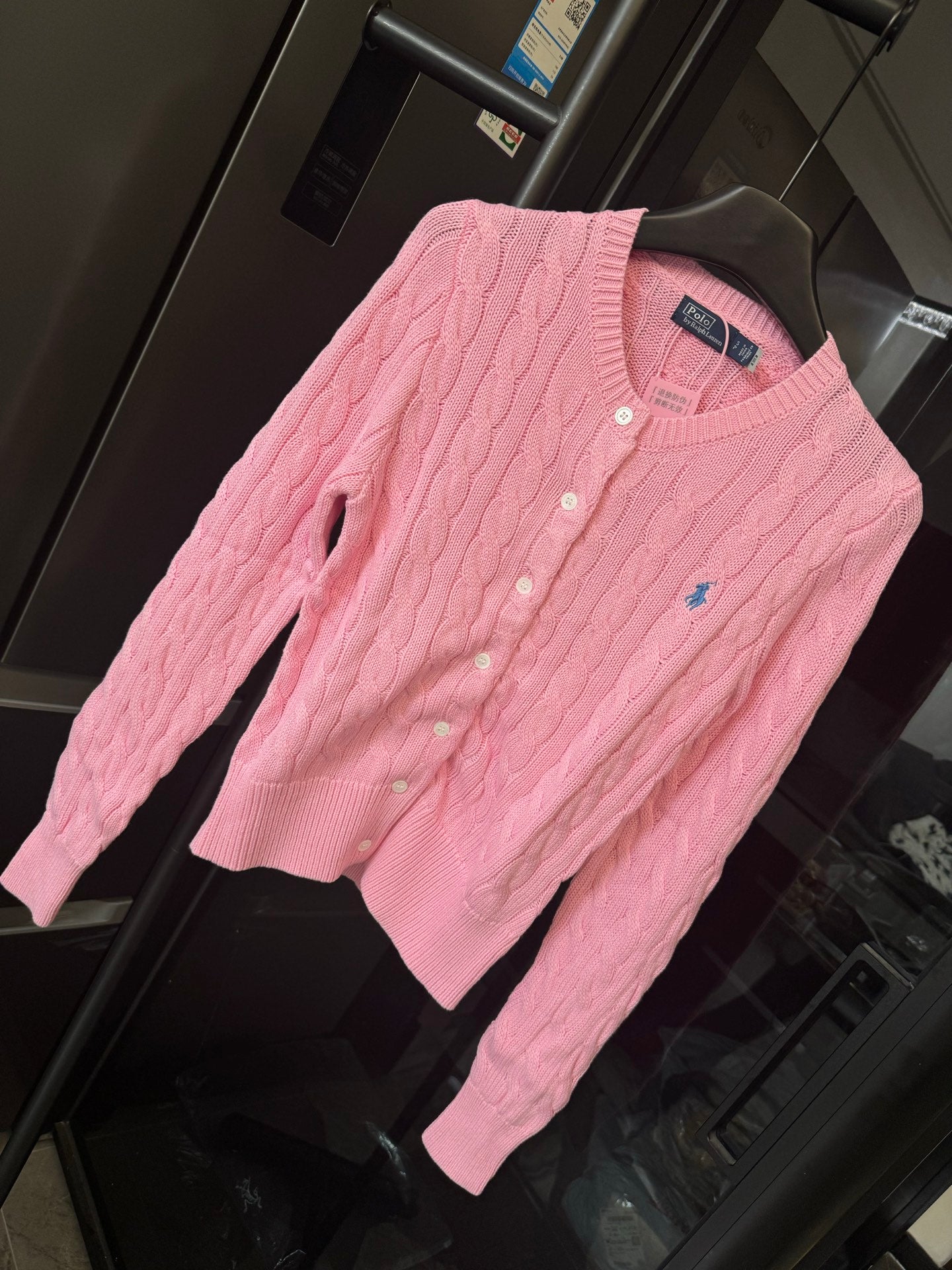 Pink cable-knit cardigan sweater with Polo logo and button placket, angled view.
