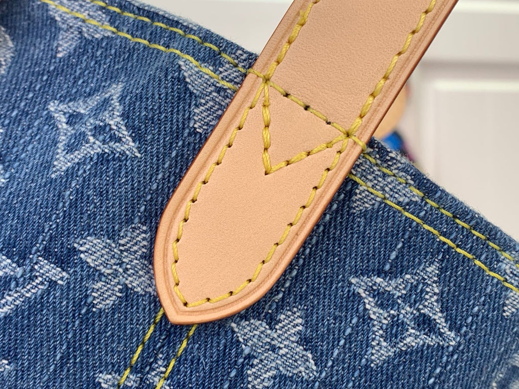 Tan leather strap tab with stitched edge on blue denim-style monogram fabric
