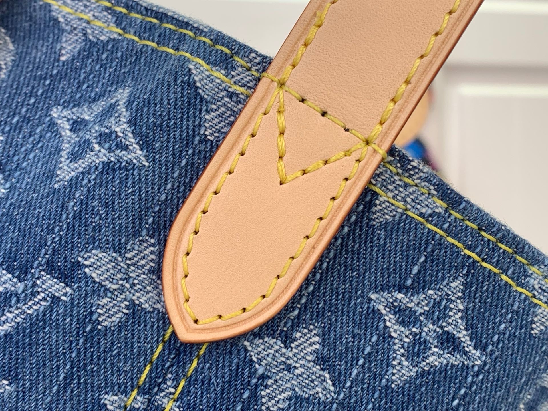 Tan leather strap tab with stitched edge on blue denim-style monogram fabric