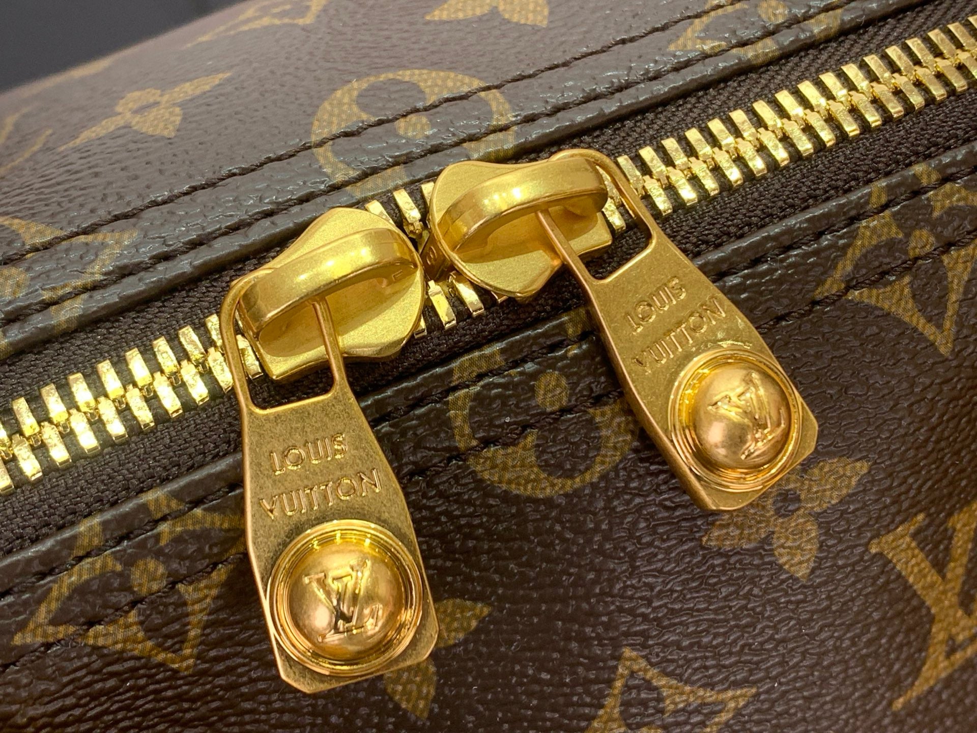 Louis Vuitton monogram bag zipper with gold-tone pull and metal slider hardware.