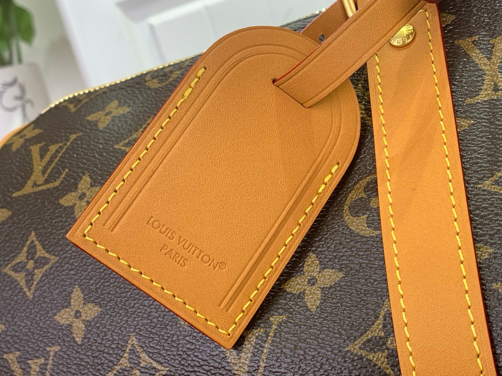 Louis Vuitton leather luggage tag with tan stitching on monogram duffel strap.