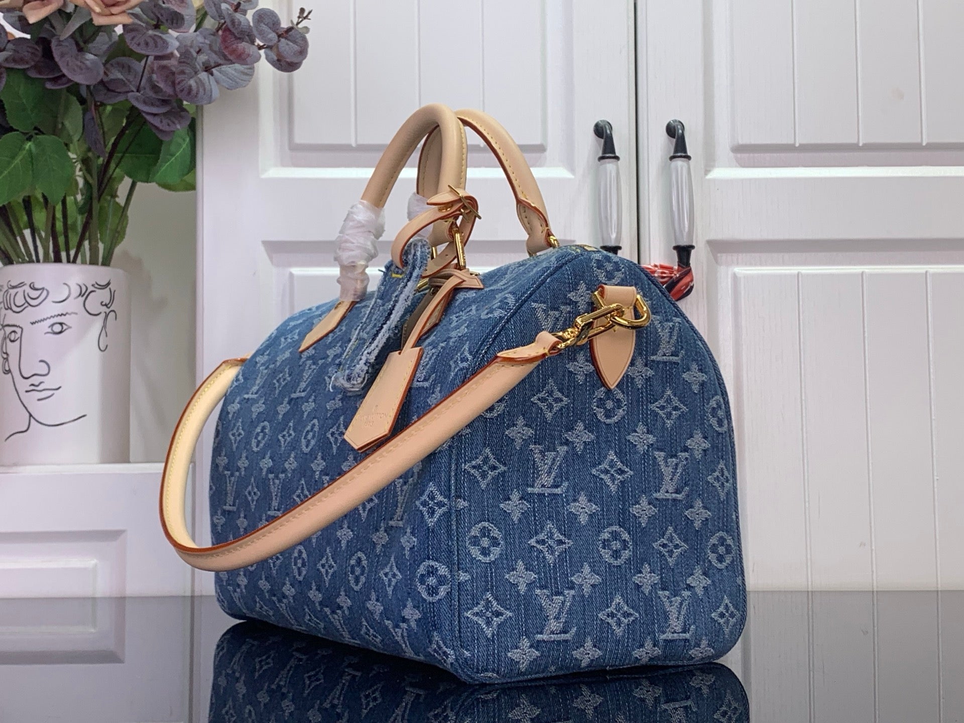 Louis Vuitton blue monogram handbag shown from the side with tan strap and gold rings