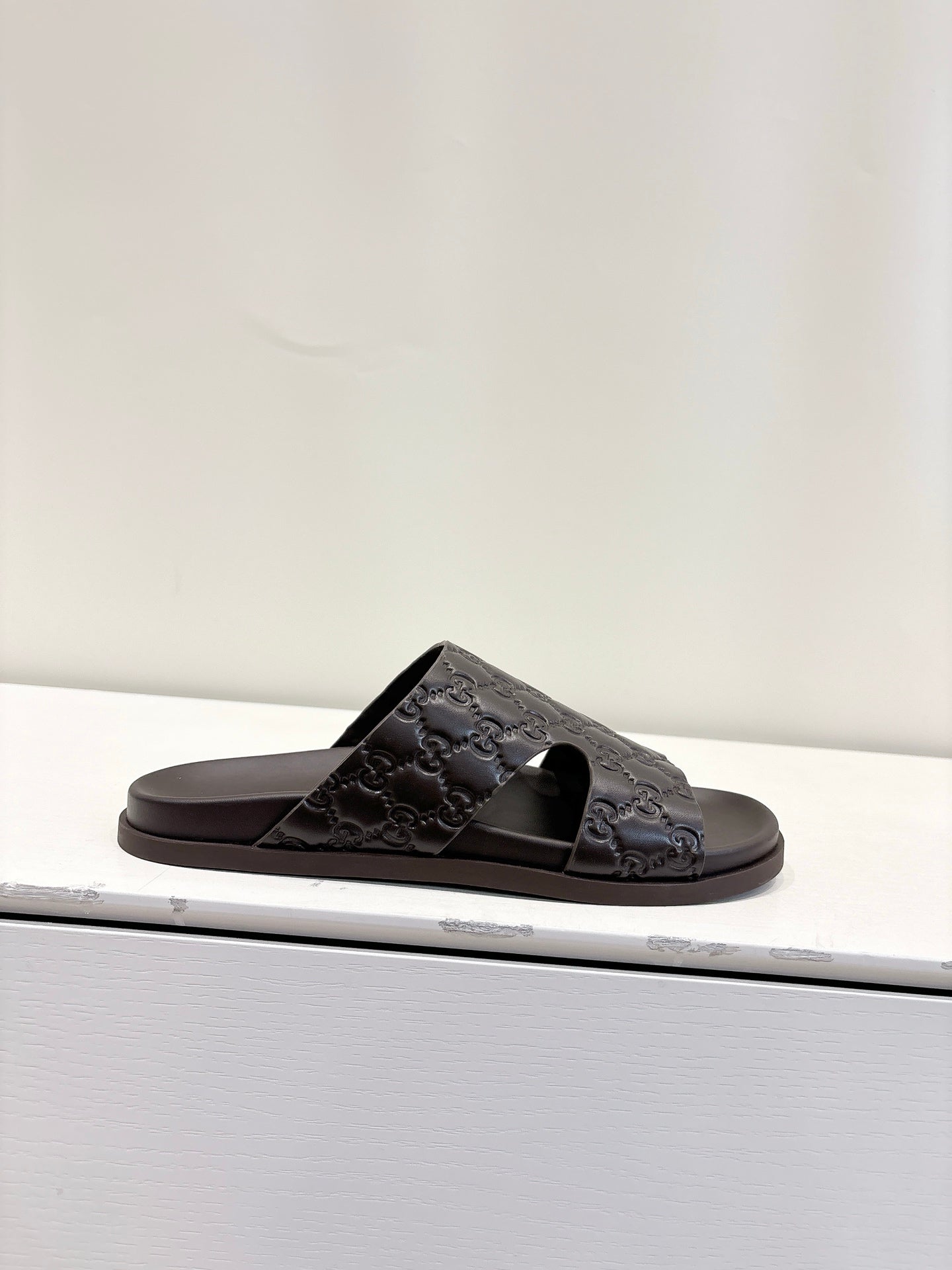 Gucci dark brown embossed slide sandal on display, open toe and logo strap