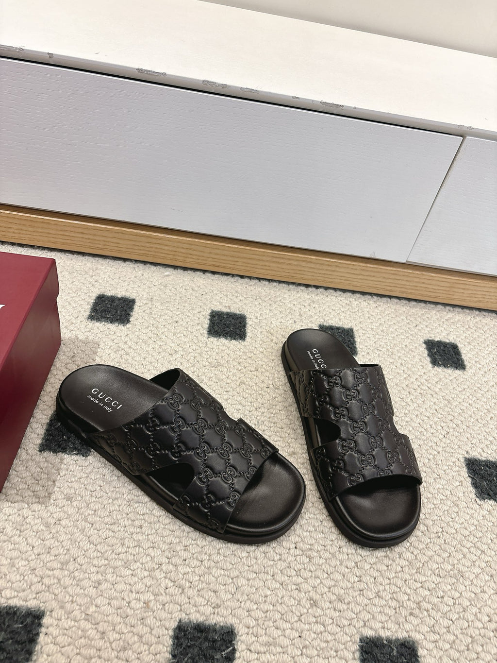 Gucci black slide sandals with embossed logo pattern across strap