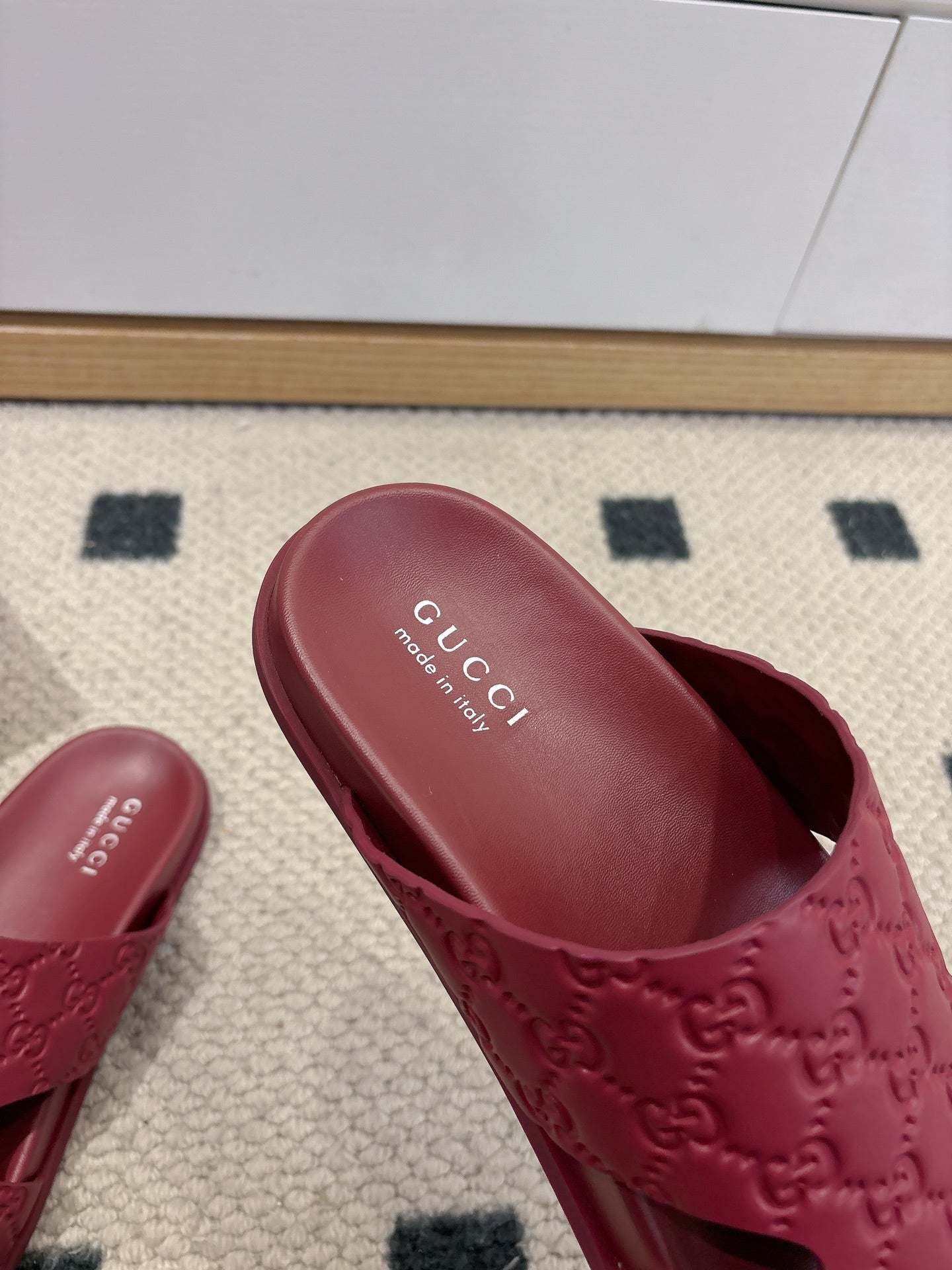 Close-up of burgundy Gucci slide sandal with embossed GG upper and branded insole