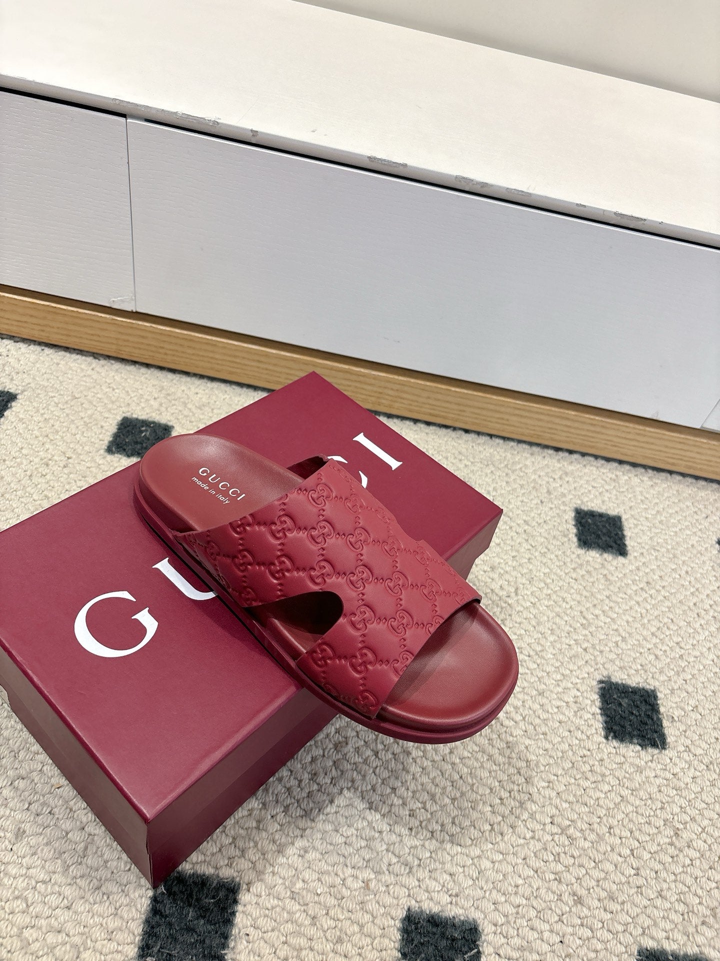 Burgundy Gucci slide sandals with embossed GG pattern and open toe on a box