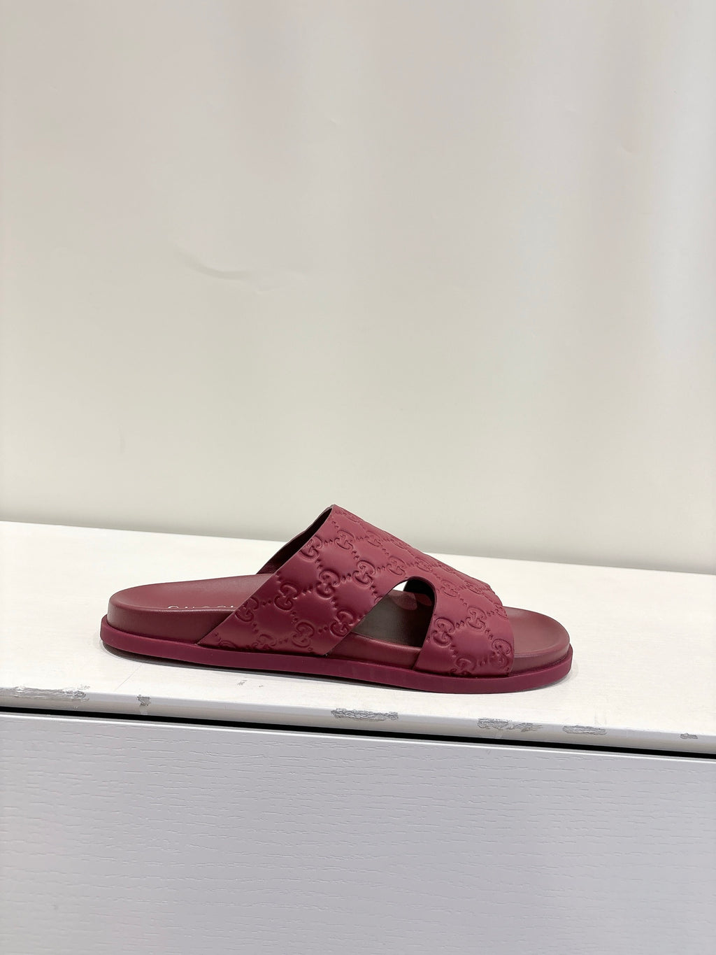Burgundy Gucci GG slide sandal on a display shelf, open toe and low profile