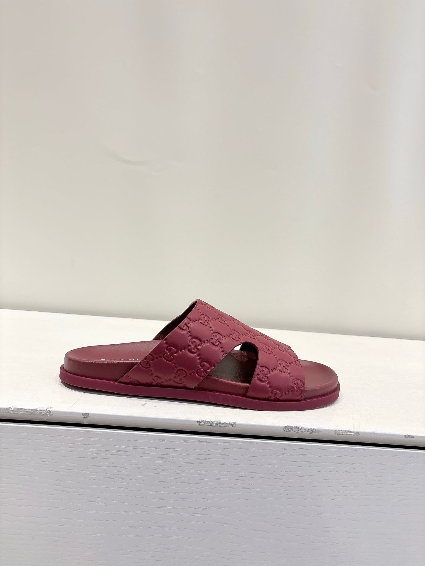 Burgundy Gucci GG slide sandal on a display shelf, open toe and low profile