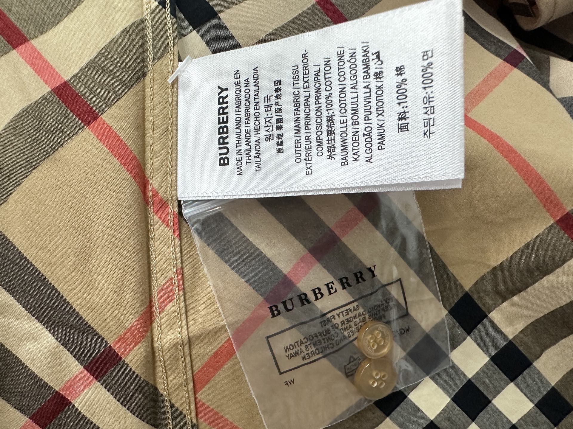 Burberry garment label and care tag on beige plaid fabric with black and red lines