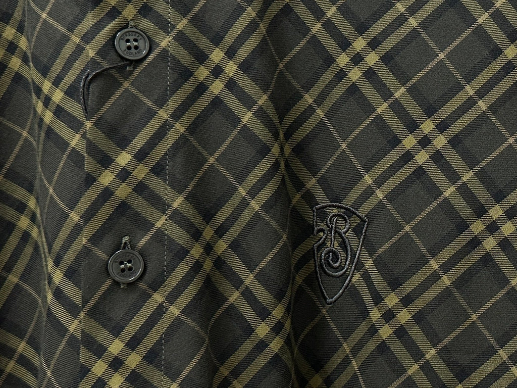 Close-up of plaid shirt front with dark buttons and embroidered emblem