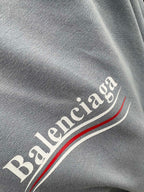 Gray fabric close-up with Balenciaga lettering and red-and-white stripe detail.