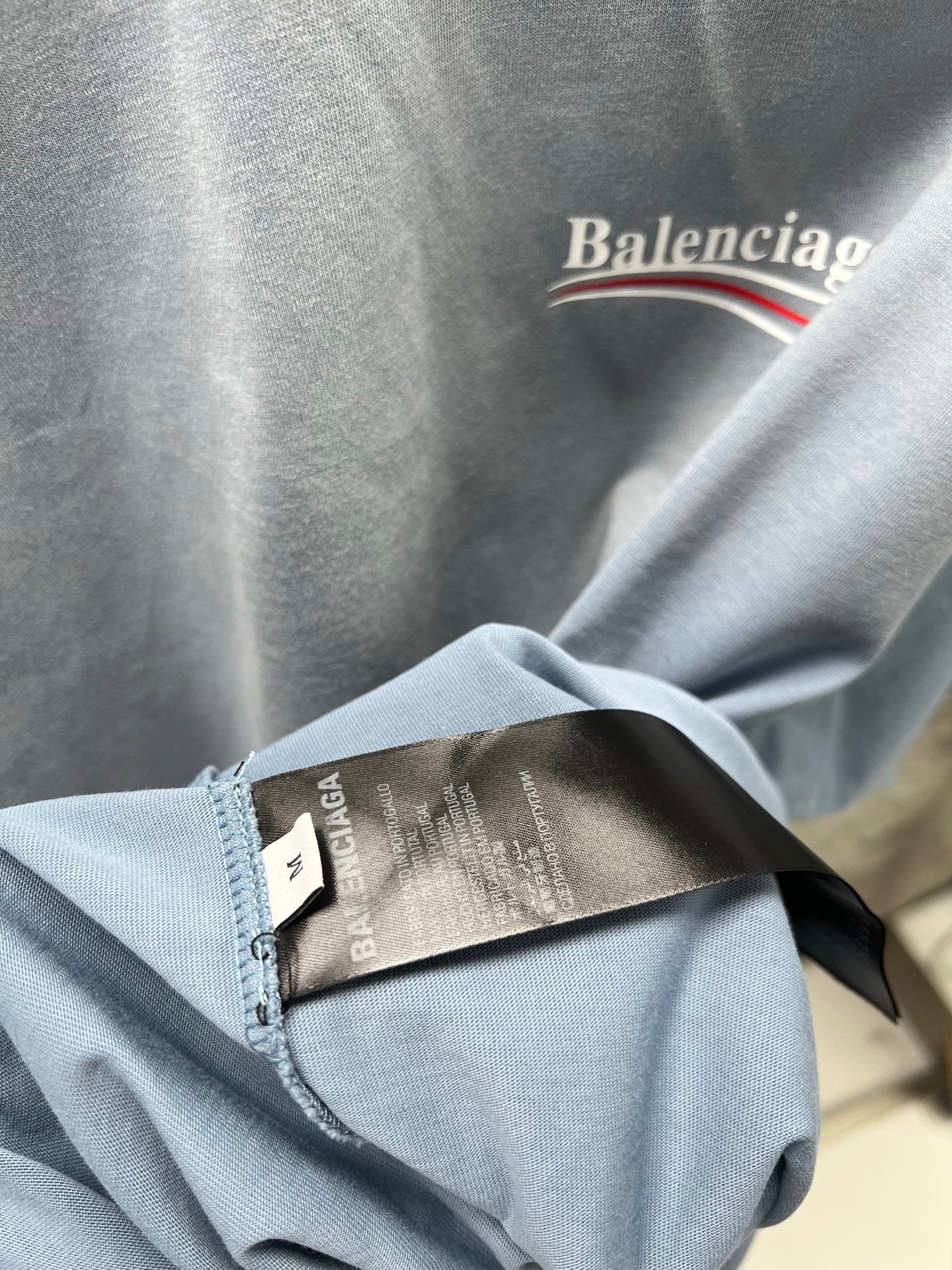 Light blue T-shirt fabric fold with inner label tag and stitching detail.