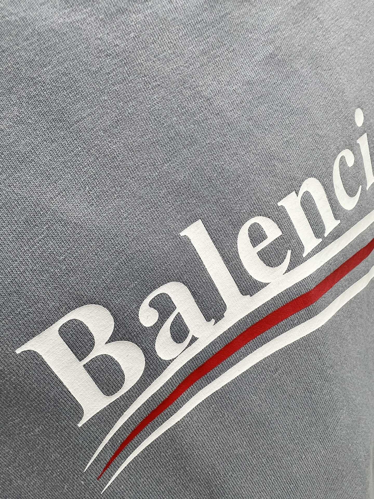 Gray fabric close-up with Balenciaga text and red-and-white stripe detail.