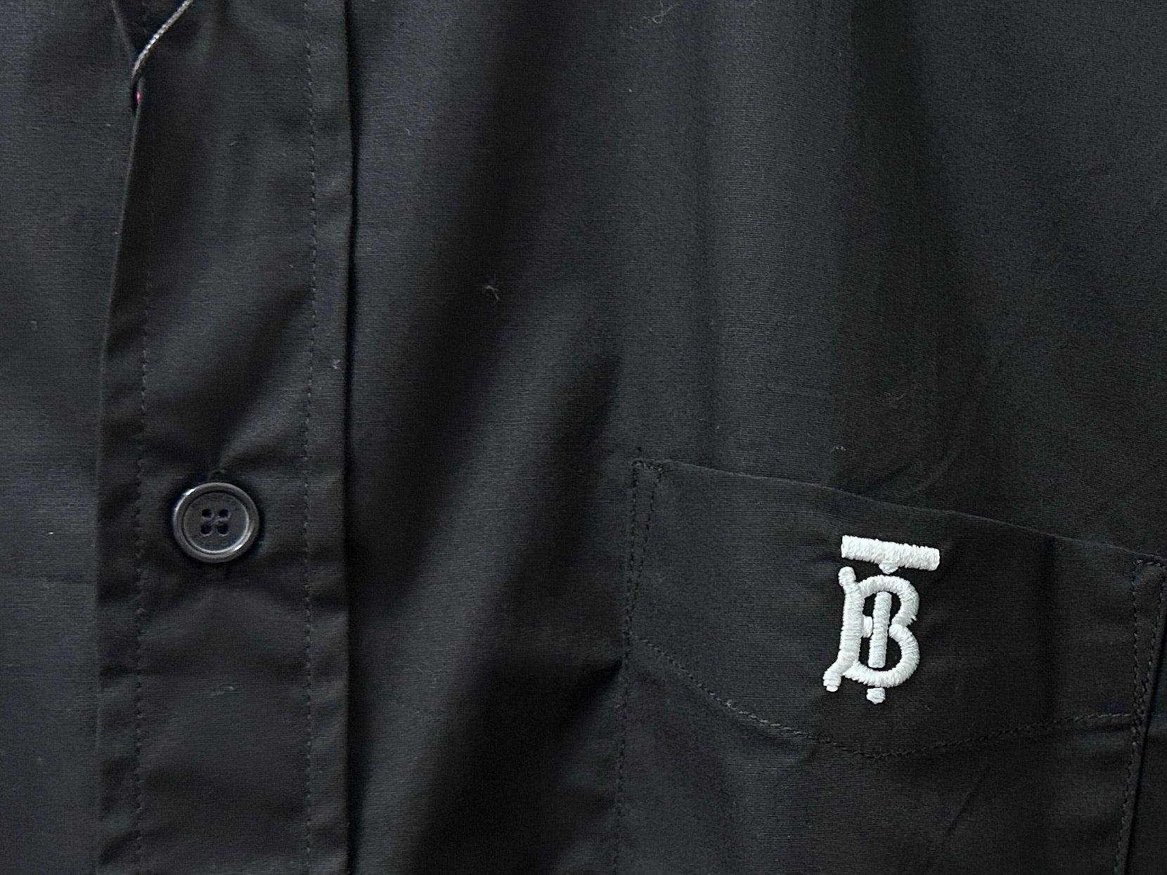 Long-sleeve button-up shirt detail: chest pocket with logo and round button