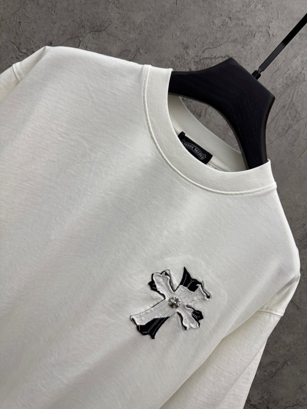 White short-sleeve T-shirt close-up at collar with small embroidered cross on chest.