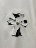 White T-shirt close-up of embroidered cross with gold-tone center detail.