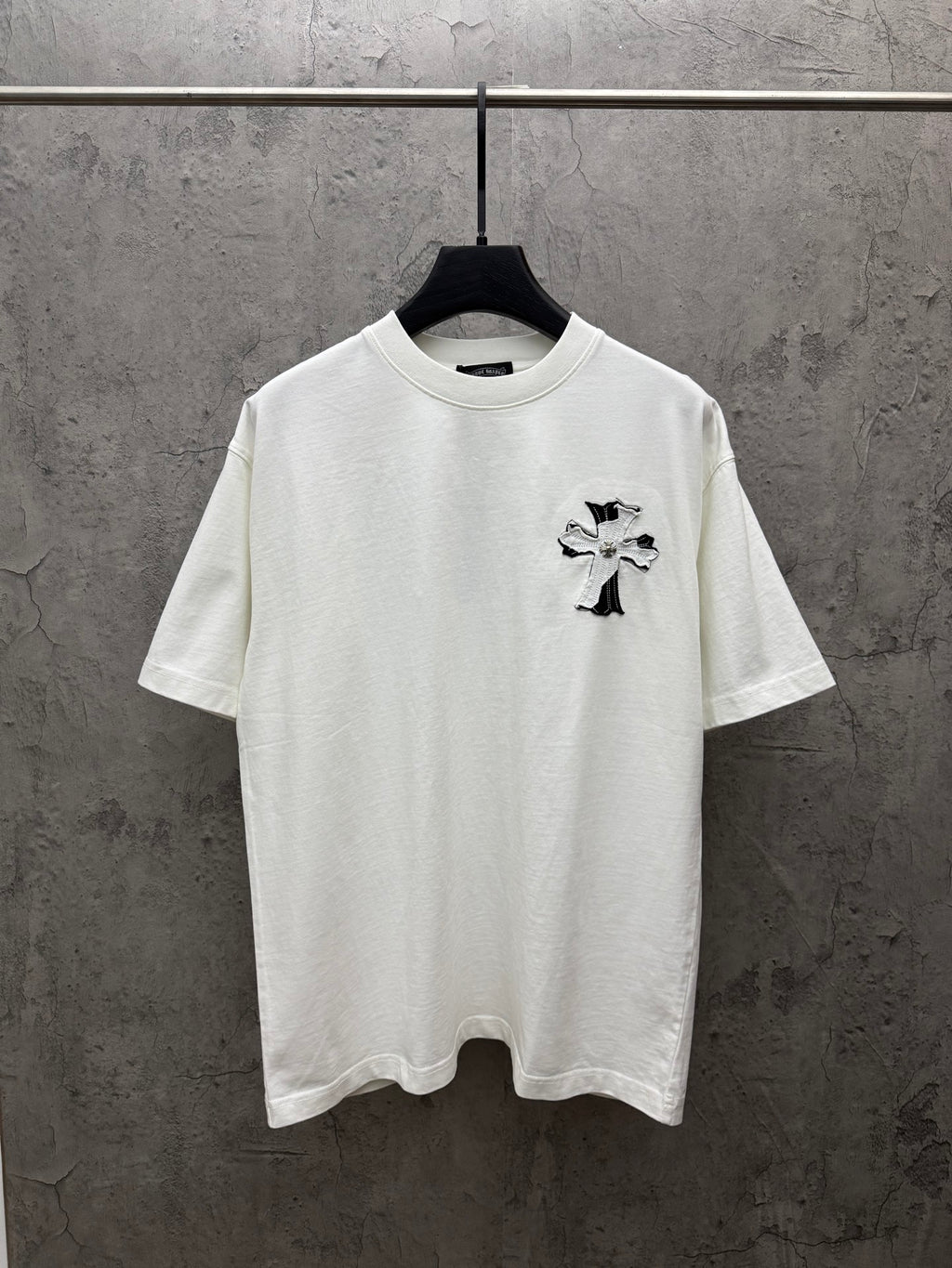 White short-sleeve T-shirt with small black-and-silver cross graphic on chest