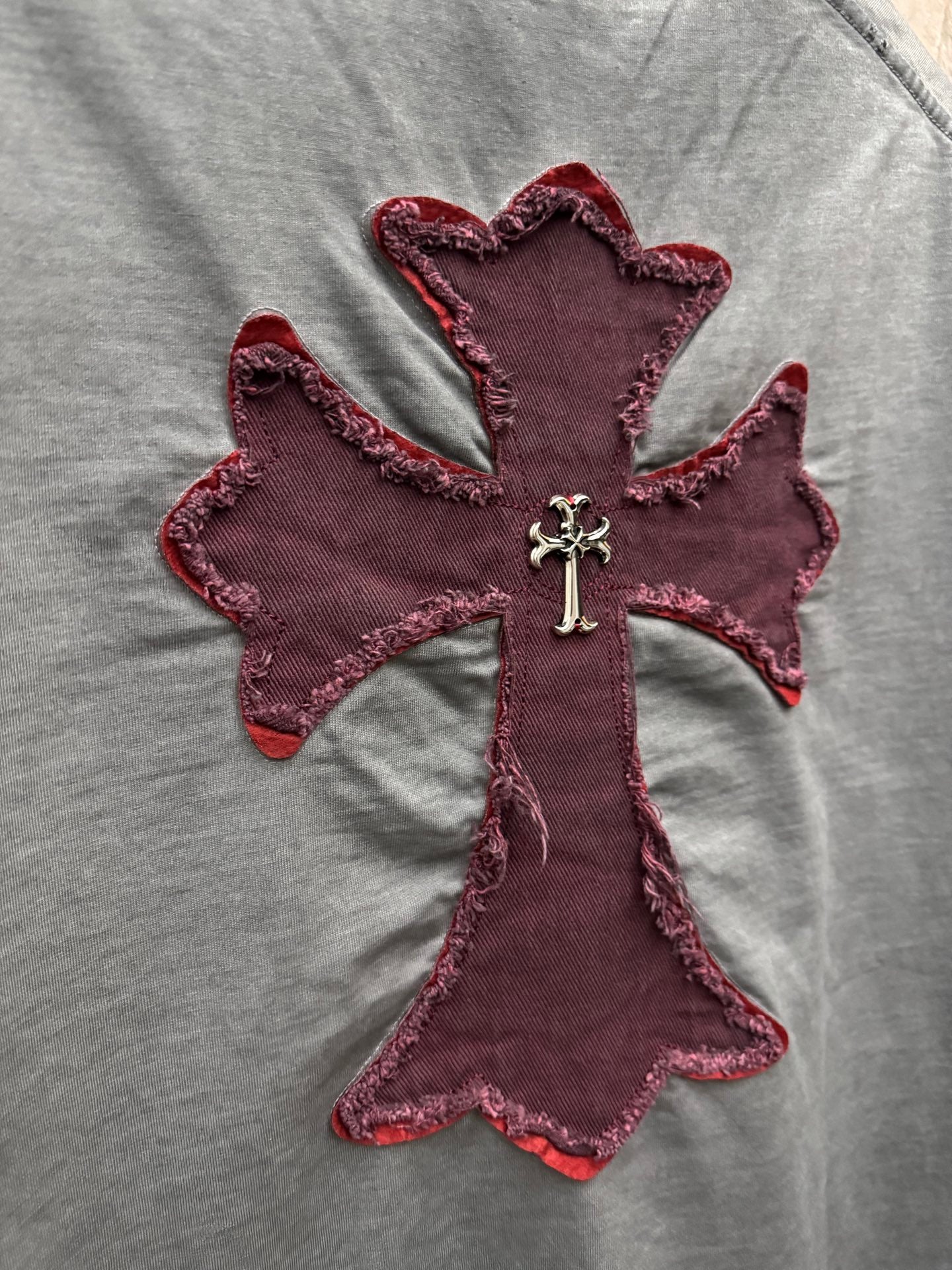Grey T-shirt close-up of maroon cross applique with silver cross emblem