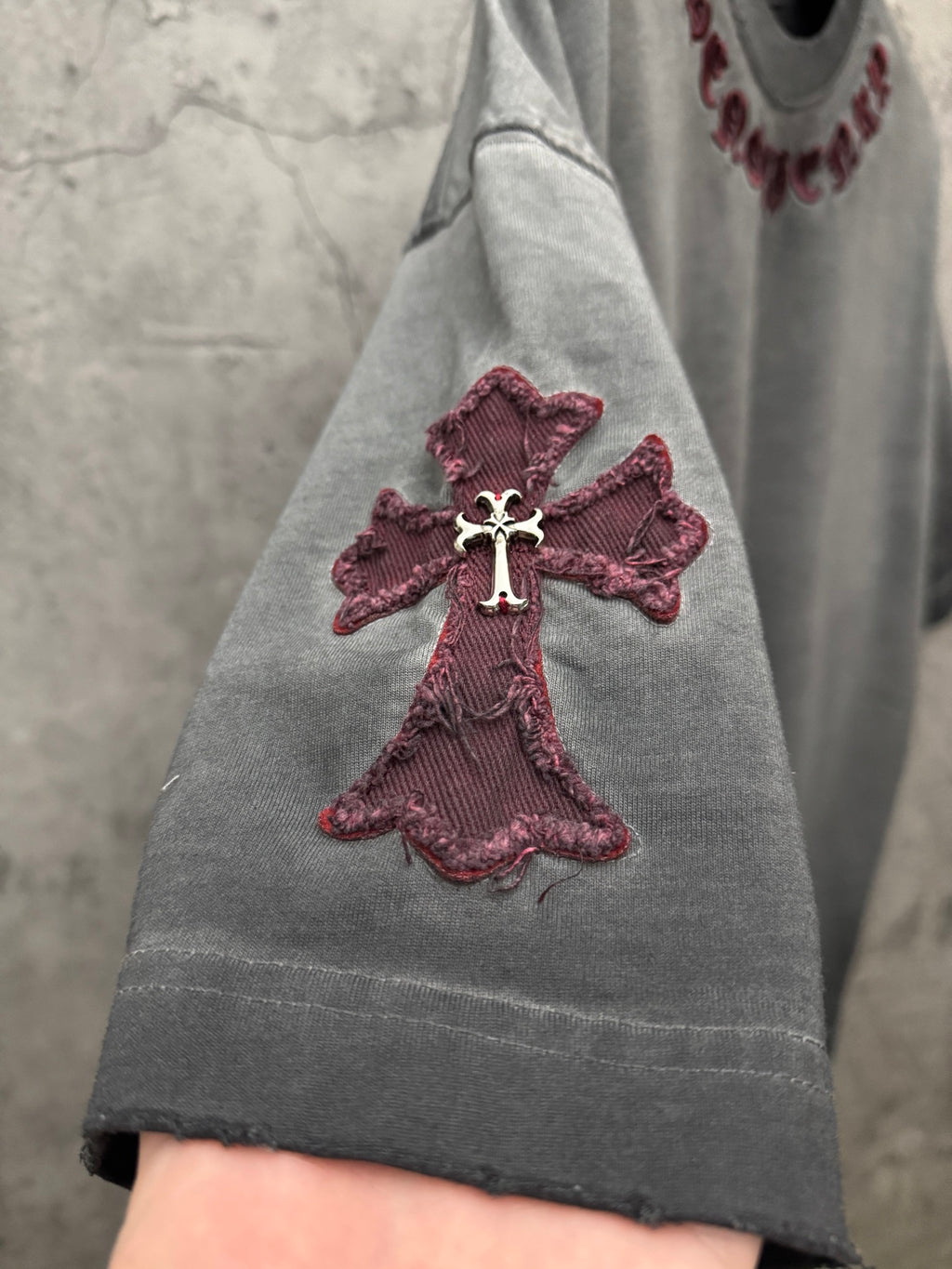 Grey T-shirt sleeve with maroon cross applique and visible seam stitching