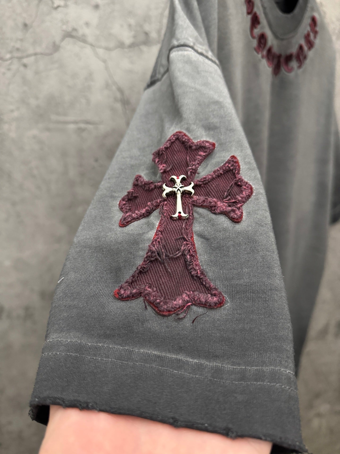 Grey T-shirt sleeve with maroon cross applique and visible seam stitching