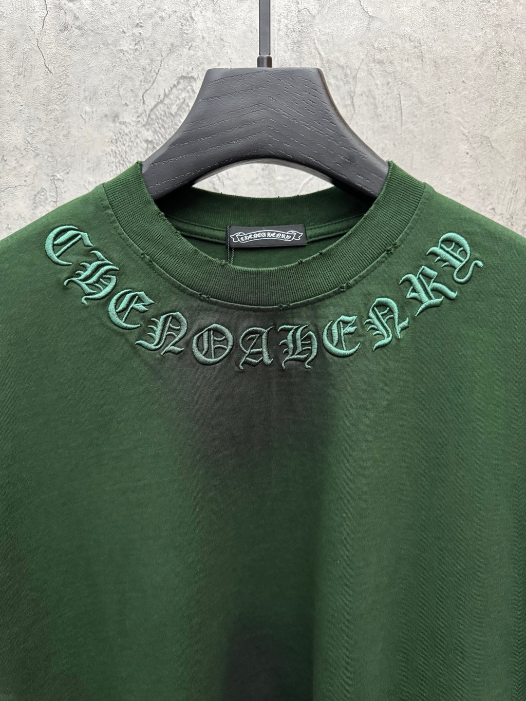 Green short-sleeve T-shirt close-up of crew neck with arched embroidered graphic