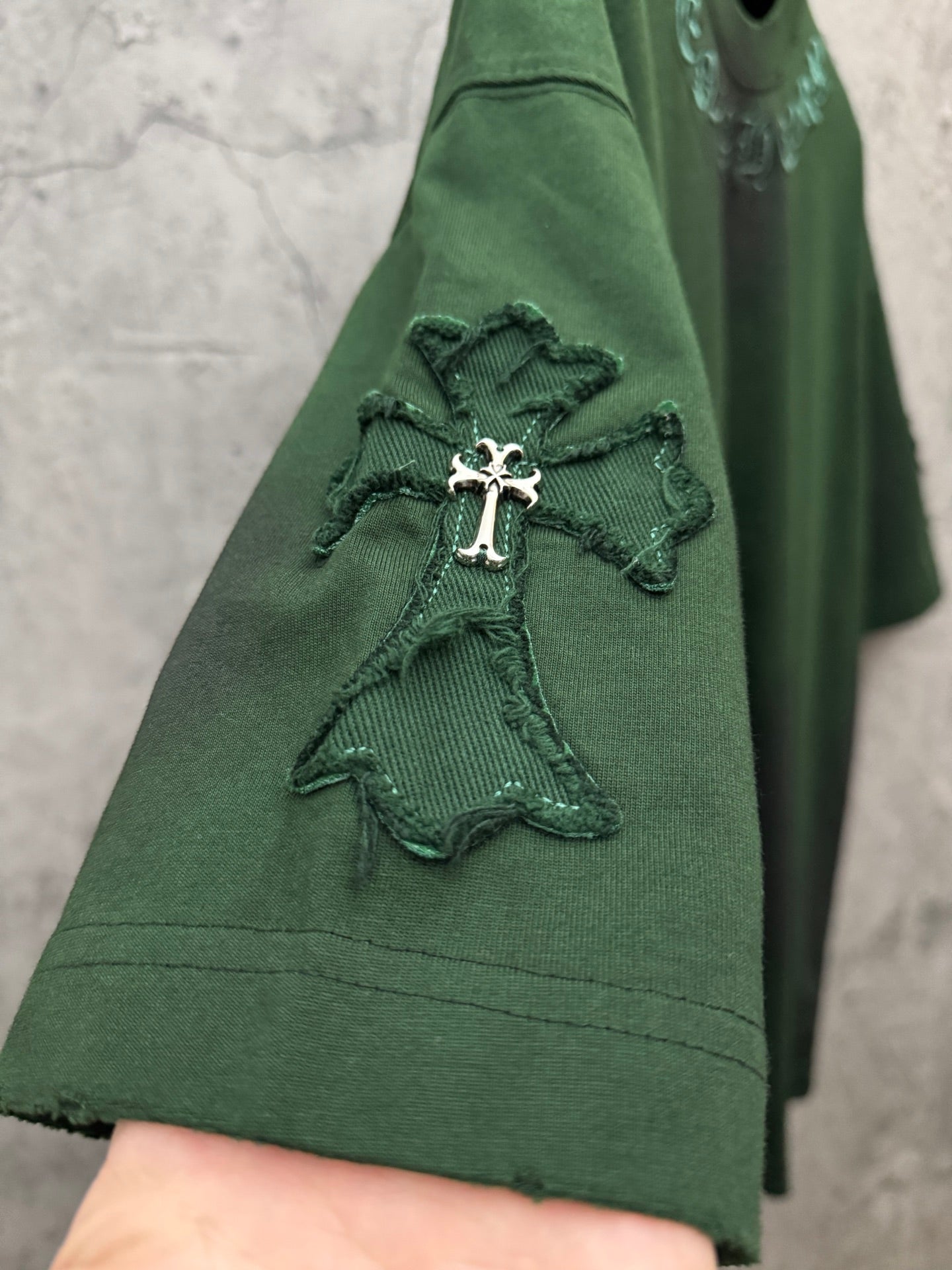 Green short-sleeve T-shirt close-up of sleeve with small embroidered angel cross