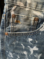 Light-wash denim jeans with bronze buttons and white speckle patches, close-up