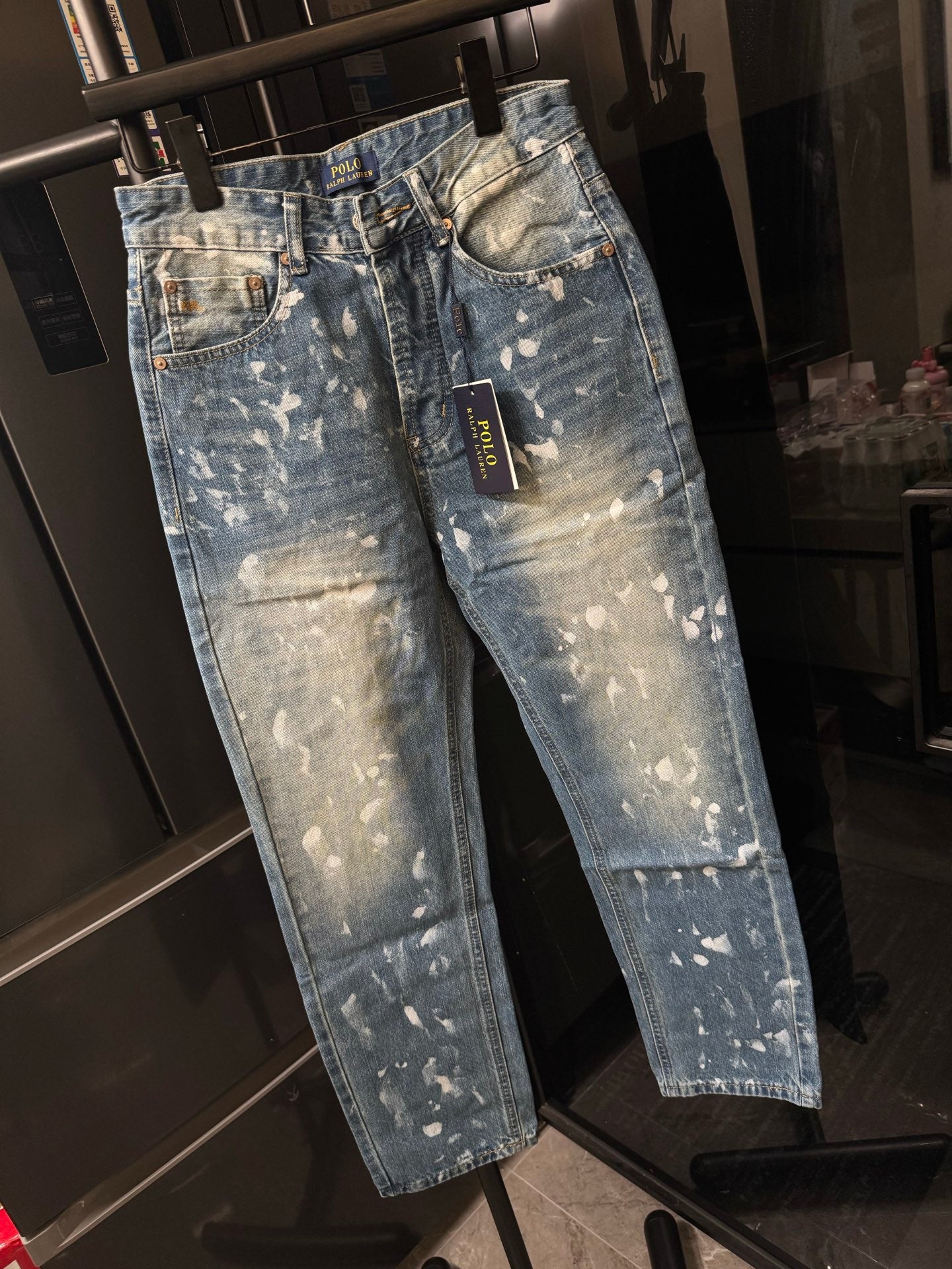 Distressed light-wash denim jeans with white splatter, angled front view