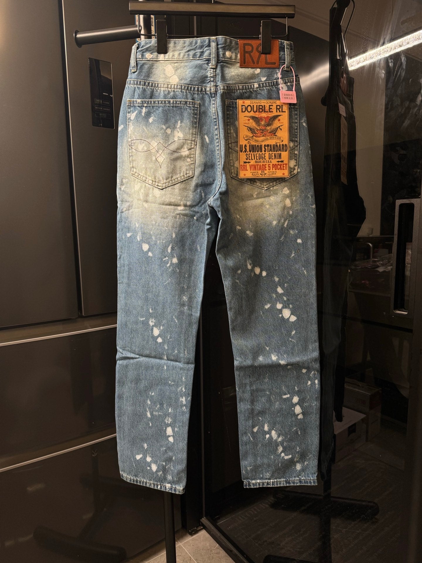 Distressed light-wash denim jeans with white speckle splatter and brand tag
