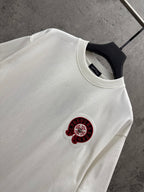 White crew-neck T-shirt with small red-and-black circular logo on chest.