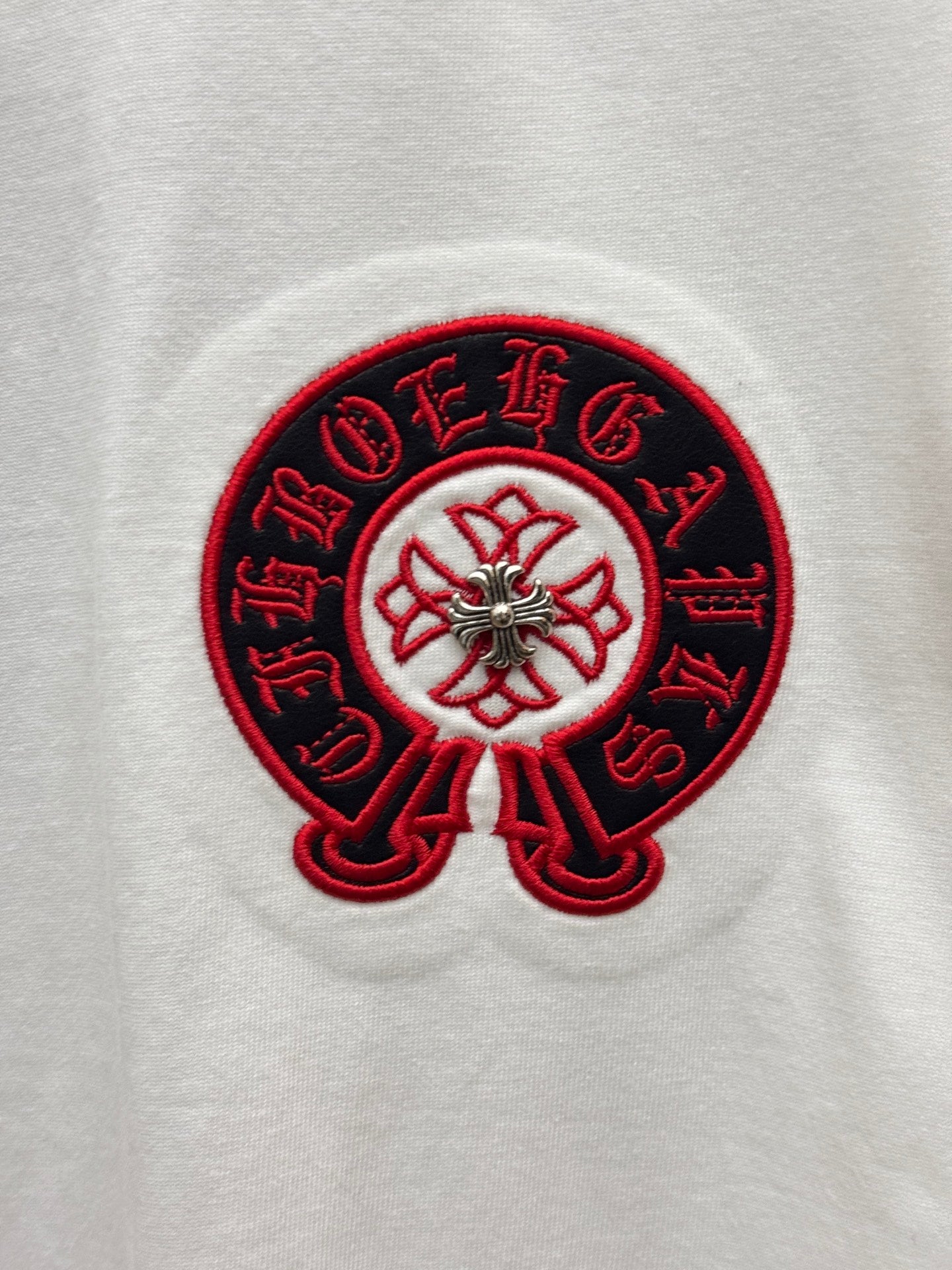 Red-and-black embroidered circular logo on white T-shirt