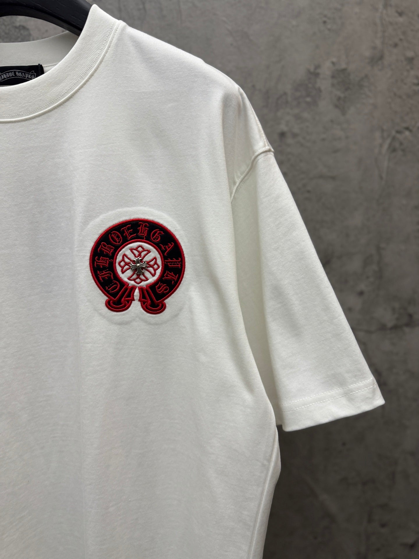White T-shirt with small red-and-black circular logo on left chest.