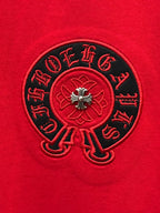 Black embroidered circular emblem with red center on red T-shirt.