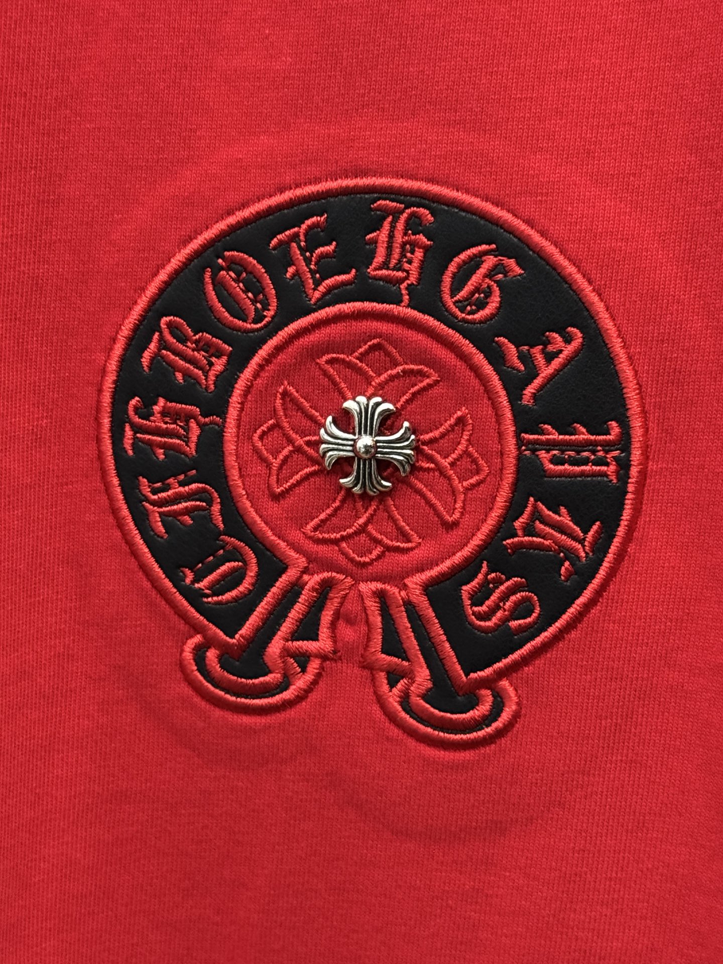 Black embroidered circular emblem with red center on red T-shirt.