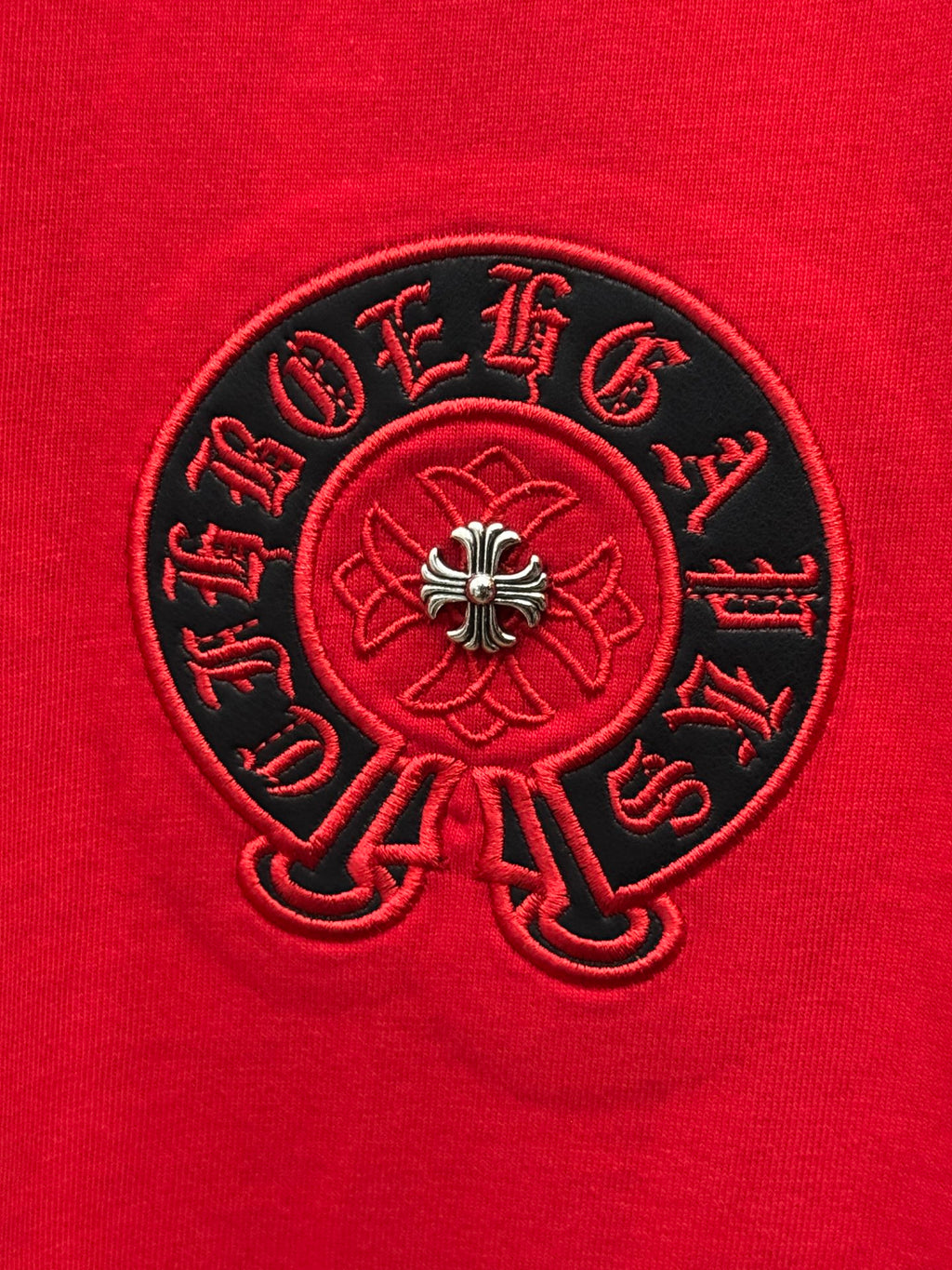Red T-shirt fabric close-up with embroidered black circular emblem