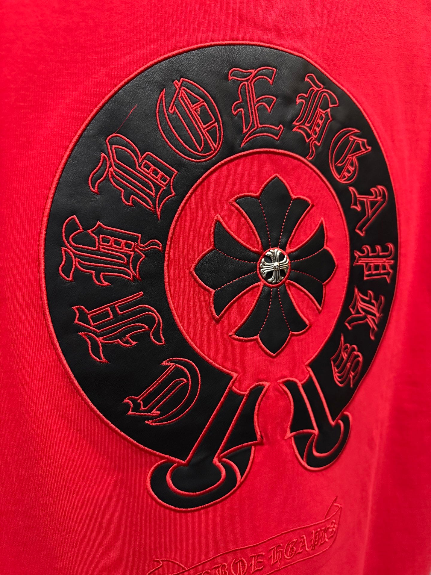 Close-up of black embroidered circular emblem on red T-shirt back.
