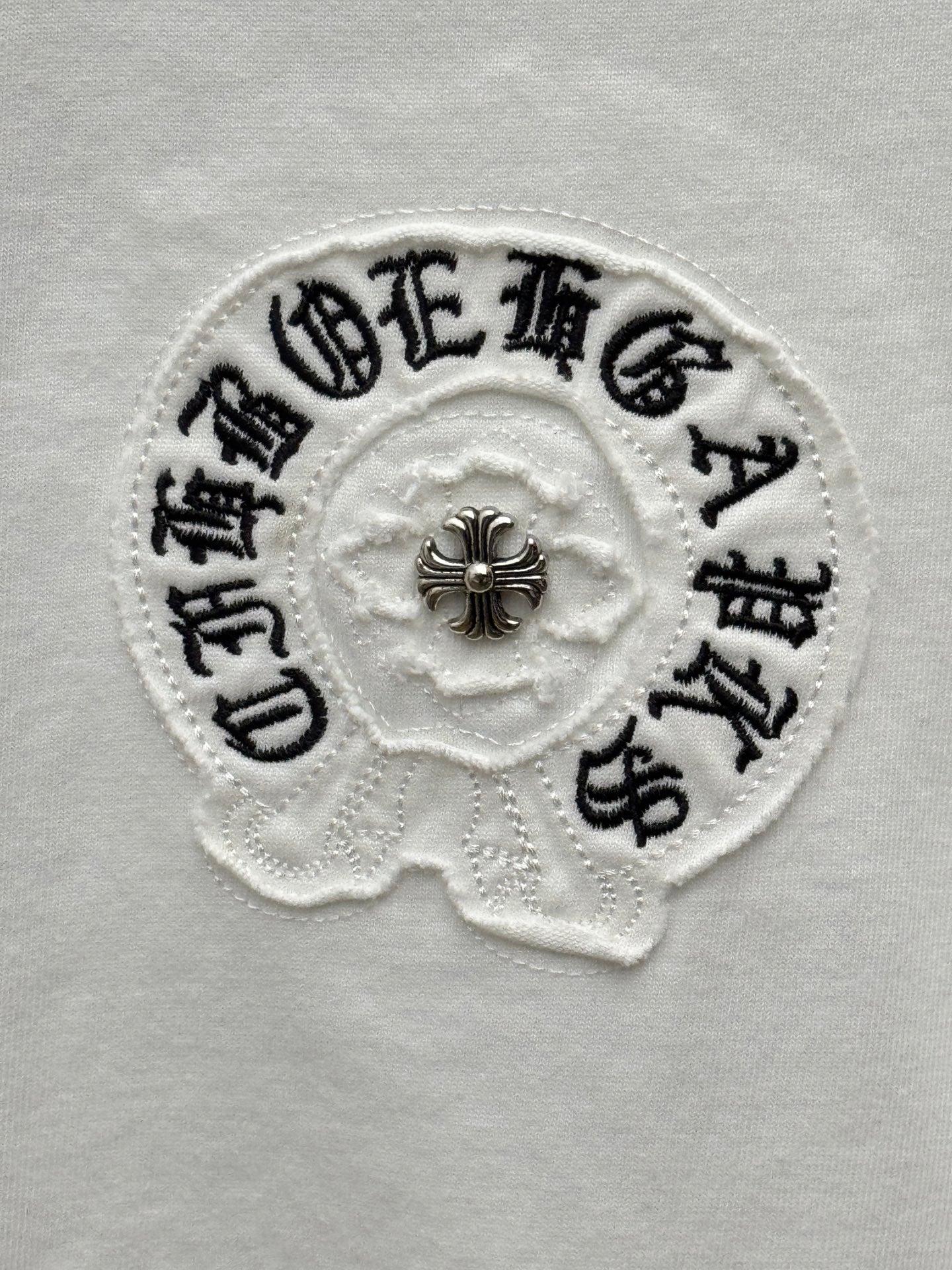 Embroidered round logo patch on white T-shirt with small cross detail
