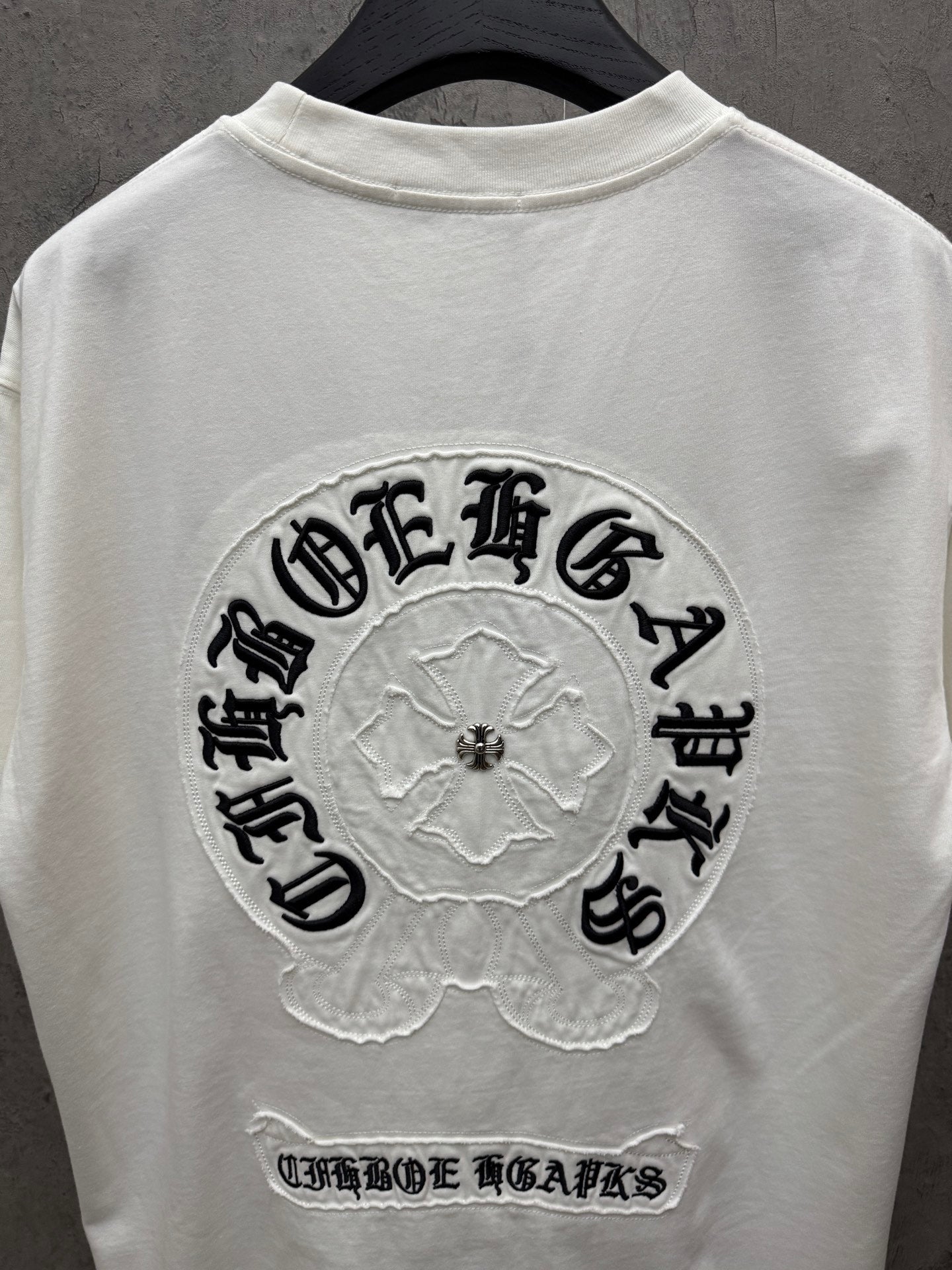 White T-shirt back view with large circular embroidered logo and small bottom text