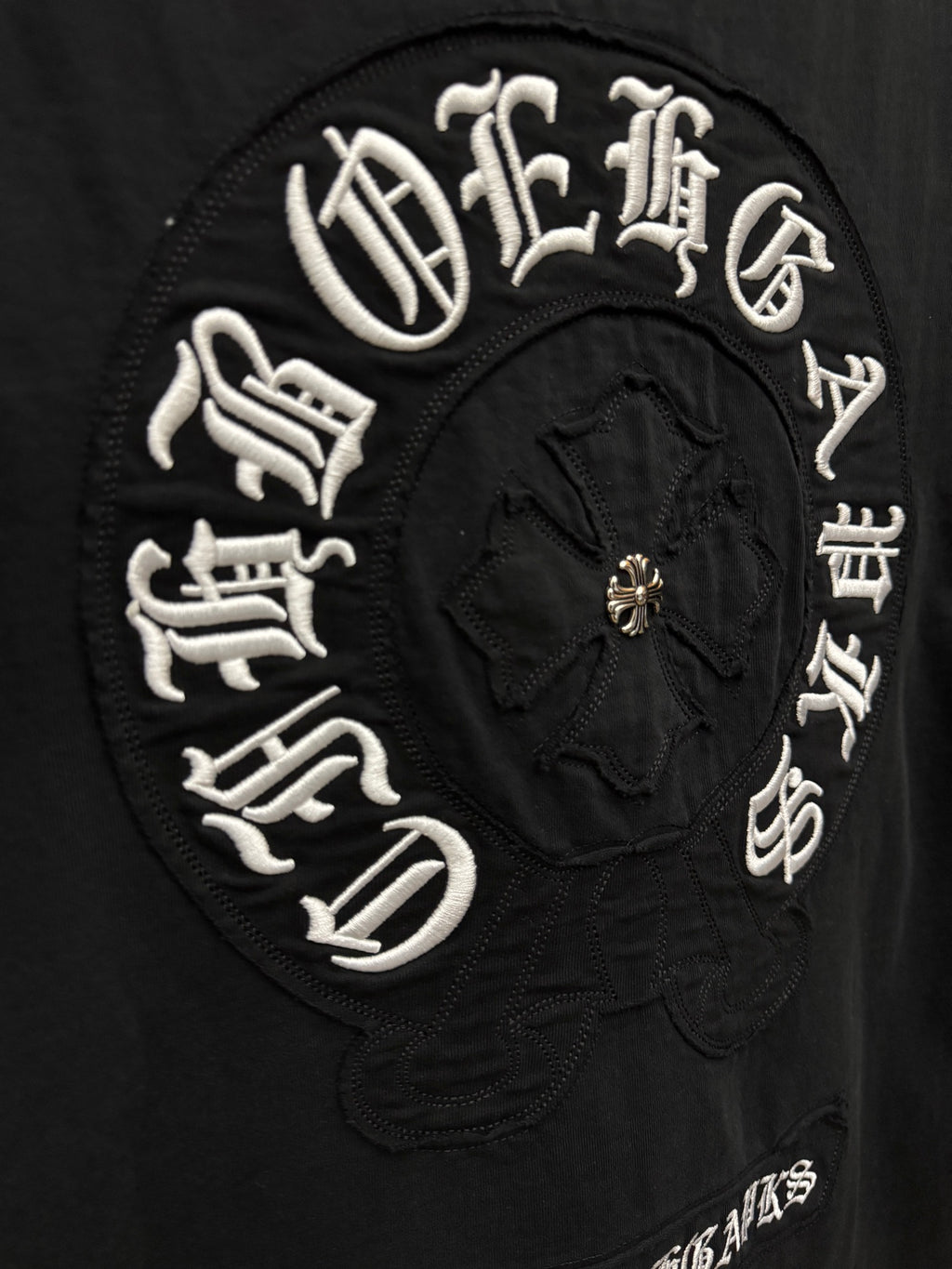 Black T-shirt close-up of circular embroidered crest with gold center detail