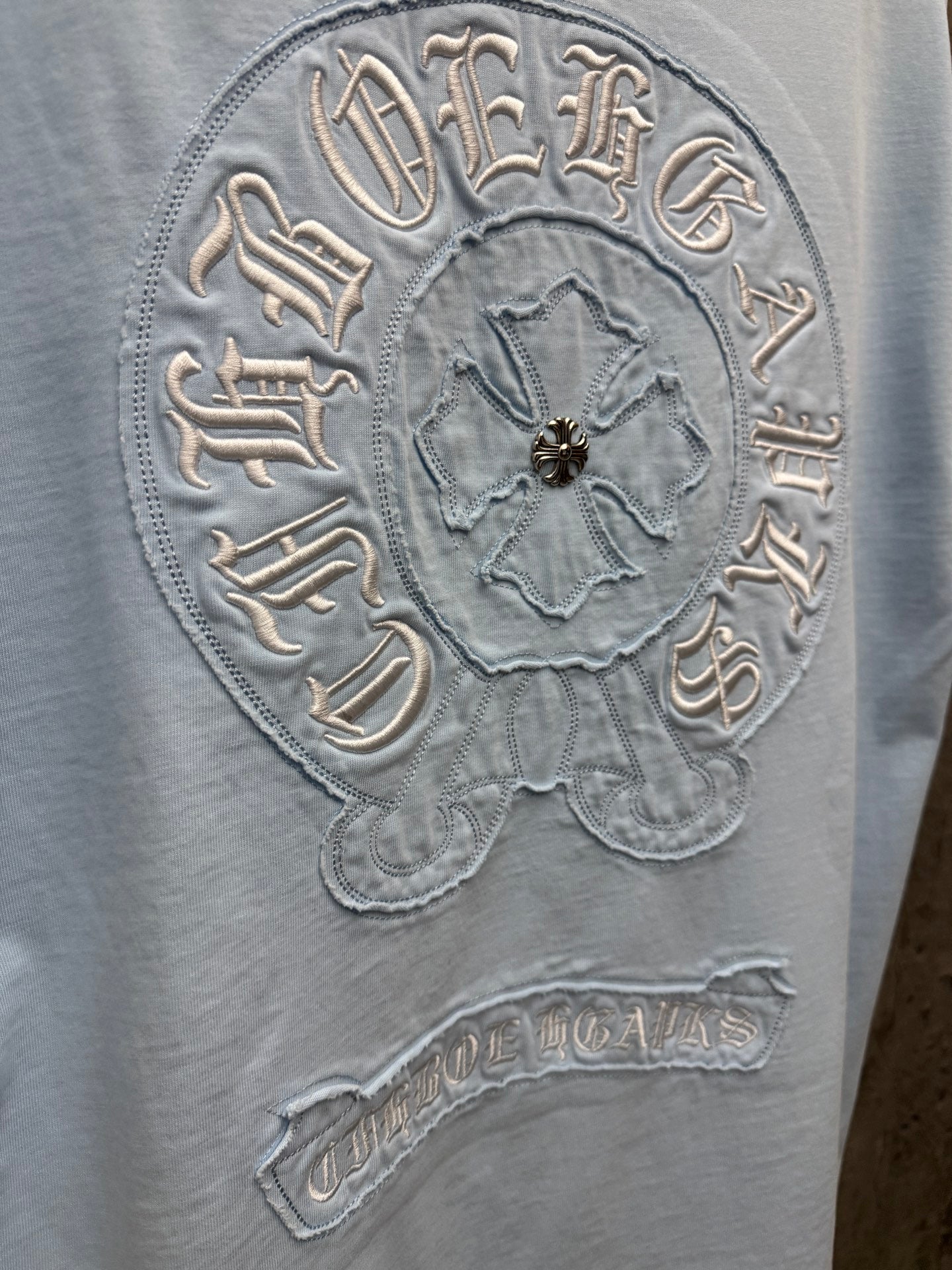 Light blue crewneck T-shirt close-up of embroidered back crest badge