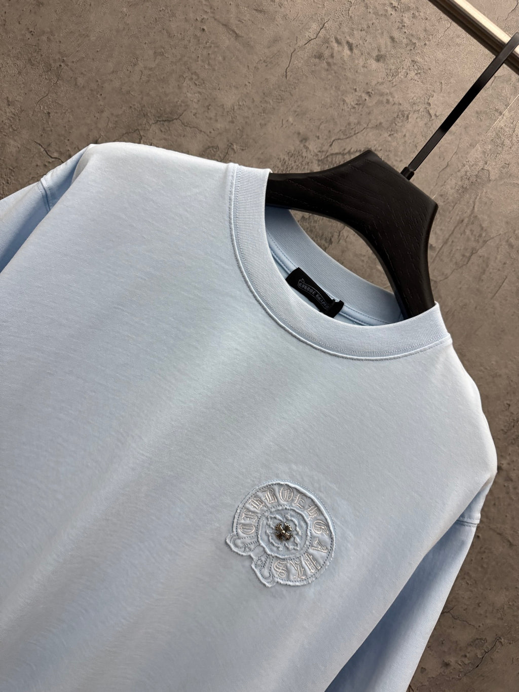 Light blue short-sleeve T-shirt close-up of crew neck and small chest embroidered badge