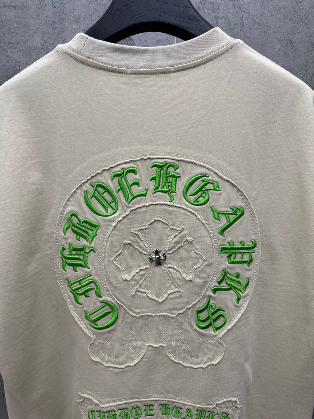 Light cream T-shirt back showing large circular green embroidered crest and text