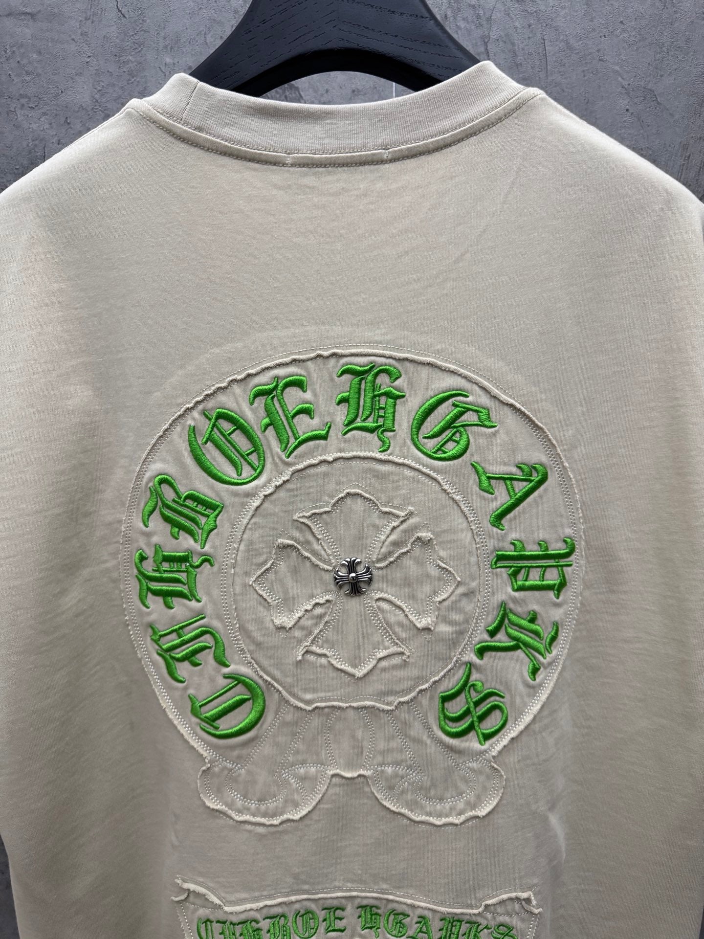 Cream T-shirt back with large green embroidered circular crest and flower motif