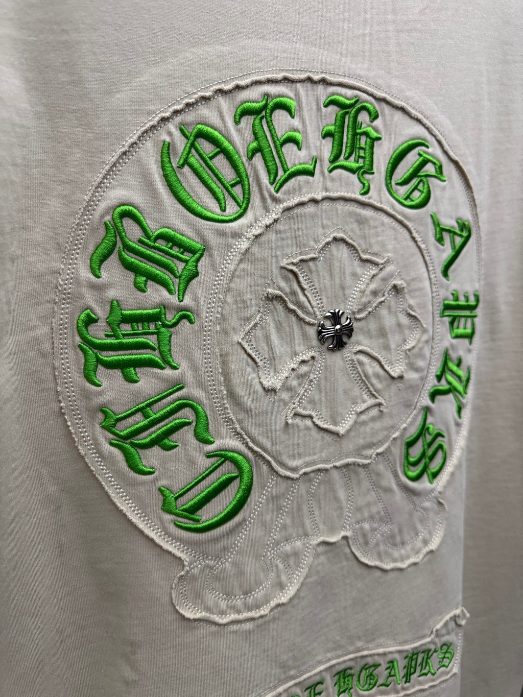 Close-up of light cream T-shirt back circular green embroidered crest with floral center