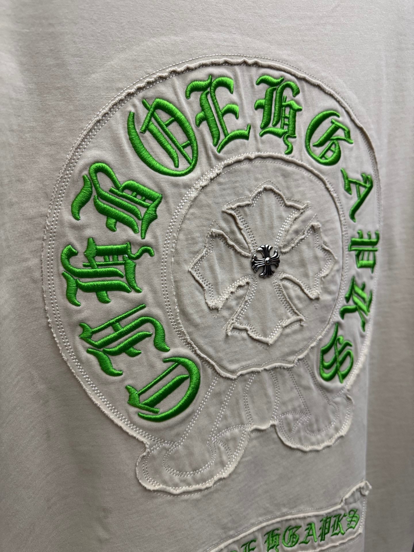Close-up of light cream T-shirt back circular green embroidered crest with floral center
