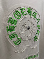Close-up of cream T-shirt back: green embroidered crest ring over gray flower