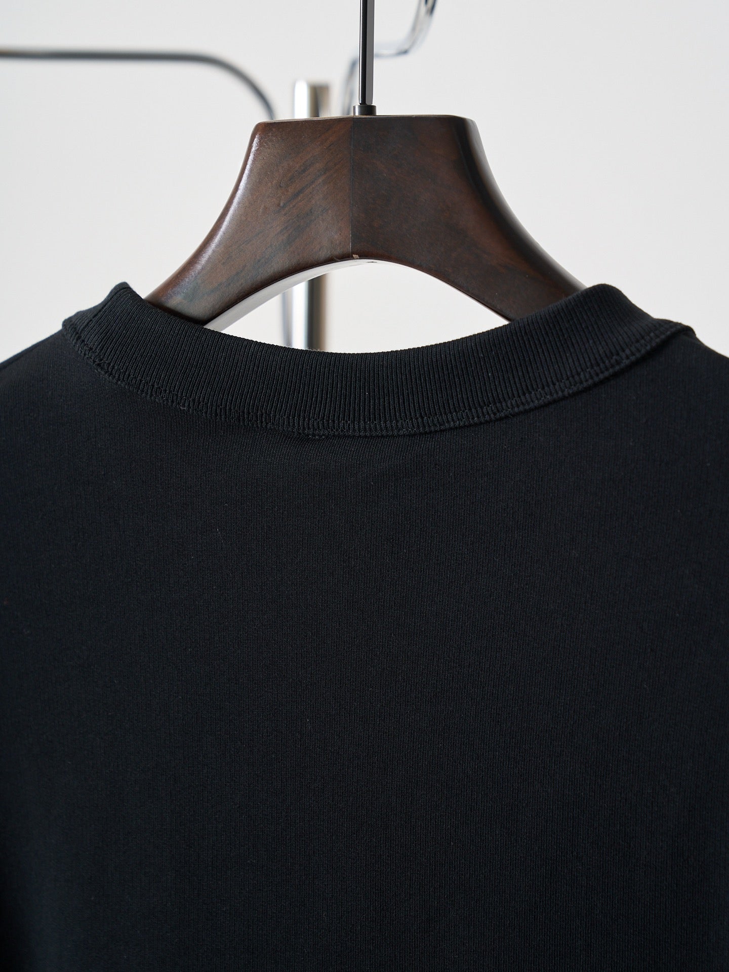 Black crewneck sweatshirt neckline detail on wooden hanger