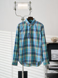 Blue-green plaid button-up shirt with pointed collar and button front on hanger