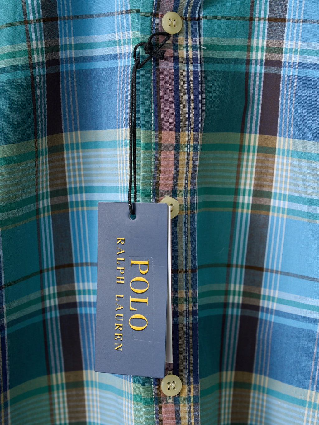 Placket buttons and hanging tag on blue-green plaid shirt